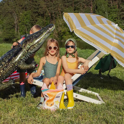 Children sitting outdoors with an umbrella and a crocodile. Kids backpack - Unicorn, featuring velvet top, waterproof bottom, adjustable straps, and zipper closure. Ideal for daycare, park, or hikes.