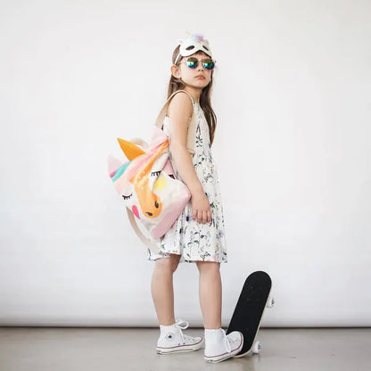 A girl wearing sunglasses holds a unicorn backpack. Kids backpack - Unicorn with velvet top, waterproof polyester bottom, adjustable straps, zipper closure. Ideal for day-care, park, or hike.