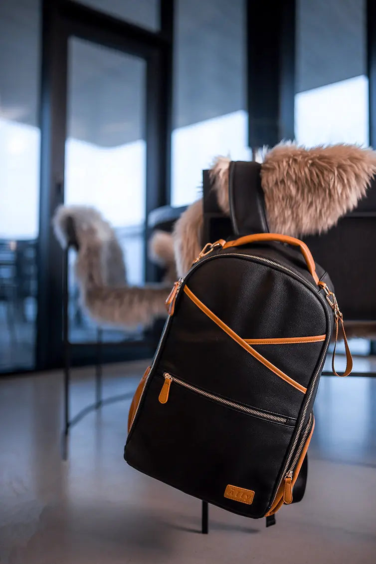 A spacious Black Coffee Diaper Backpack on a chair, featuring a furry object, stroller straps, and 16 pockets for ultimate convenience and style.