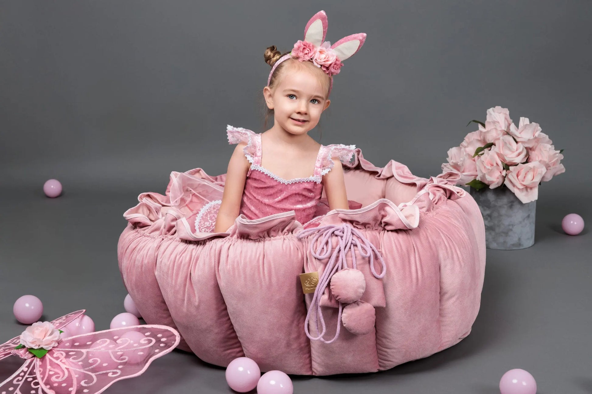 A girl in a pink dress playing with a Flower Play Mat that transforms into a ball pit, surrounded by delicate ruffle, stimulating sensory development. 100 balls included.