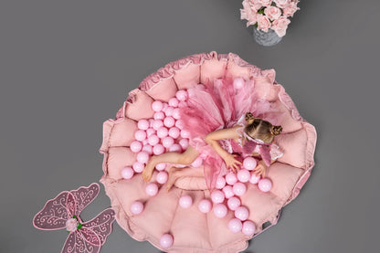 A girl in a pink dress playing on a flower-themed playmat, transforming into a ball pit. Includes 100 balls for sensory development. Made from soft cotton and polyester velvet.