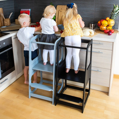 Children on a Montessori Helper Tower Step Stool in a kitchen, promoting independence and safe learning. Height-adjustable, sturdy Baltic birch plywood, handmade in Latvia. Ideal for young chefs.