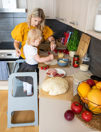 A woman and child in a kitchen using the Montessori Learning Tower Step Stool, encouraging safe exploration and independence. Adjustable design, sturdy Baltic birch plywood, handmade in Latvia.