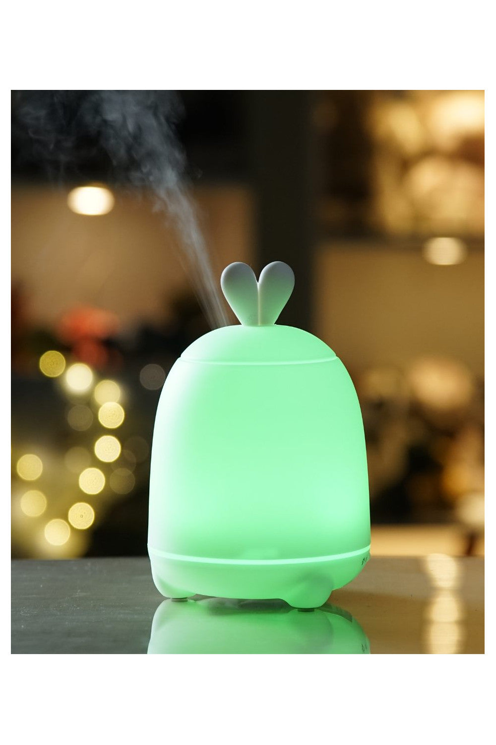 A green diffuser with rabbit ears and a white cap, emitting cool mist for air humidification and aromatherapy. LED light changes colors for night use. Dimensions: 15.1 x 10 x 10 cm.