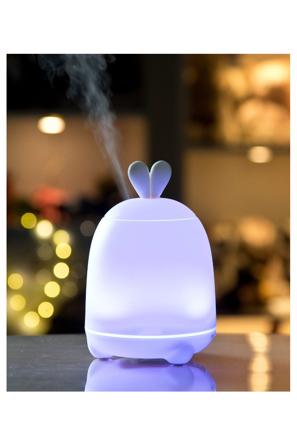 A white diffuser lamp with bunny ears, emitting cool mist and LED light. Enhances child's room humidity and sleep quality. Features color-changing light and aromatherapy function. Dimensions: 15.1 x 10 x 10 cm.