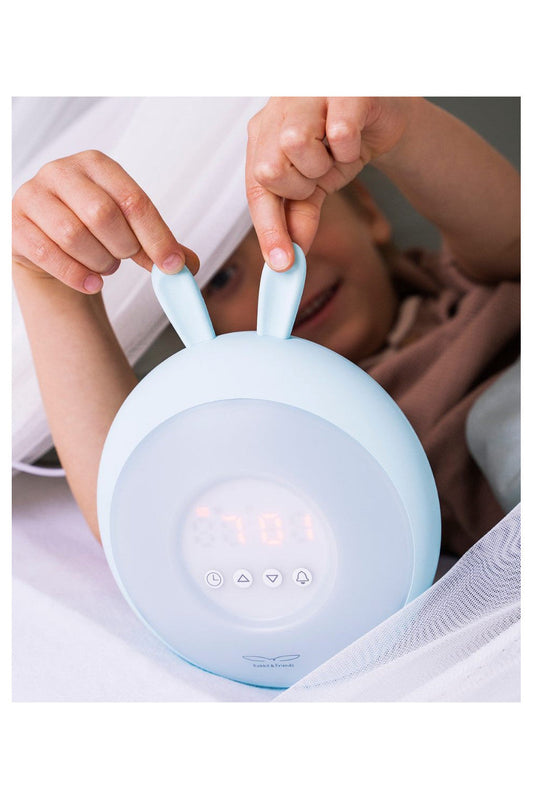 A child holds a Rabbit Lamp with Alarm Clock – Blue, featuring sunrise and sunset functions, light intensity adjustments, 5 melodies, touch control, and non-slip base feet.