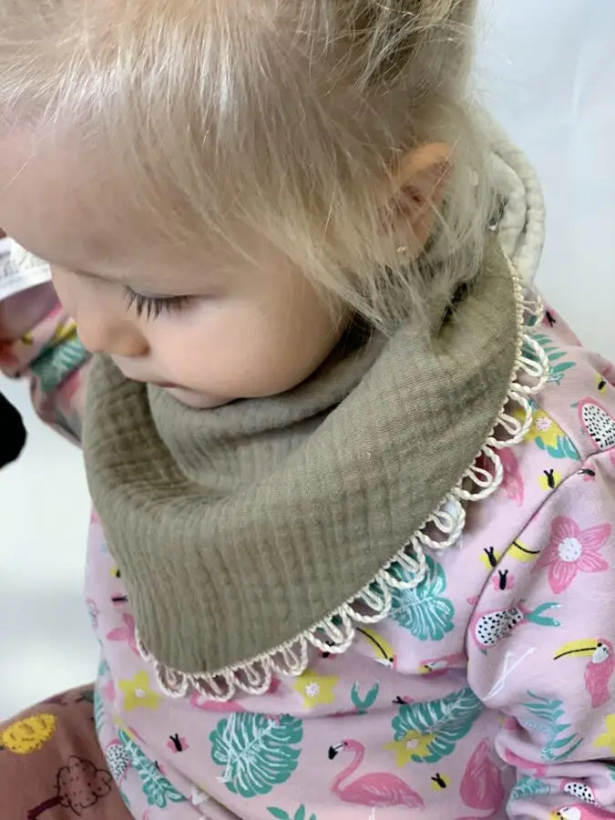 Close-up of a baby wearing a handmade double-sided muslin scarf-bib in khaki. Soft and stylish, designed for ages 6 months to 3 years.