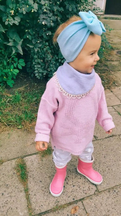 A child wearing a hat and sweater with a bow on her head, showcasing a handmade double-sided muslin Scarf-Bib - Light Blue for ages 6 months to 3 years.