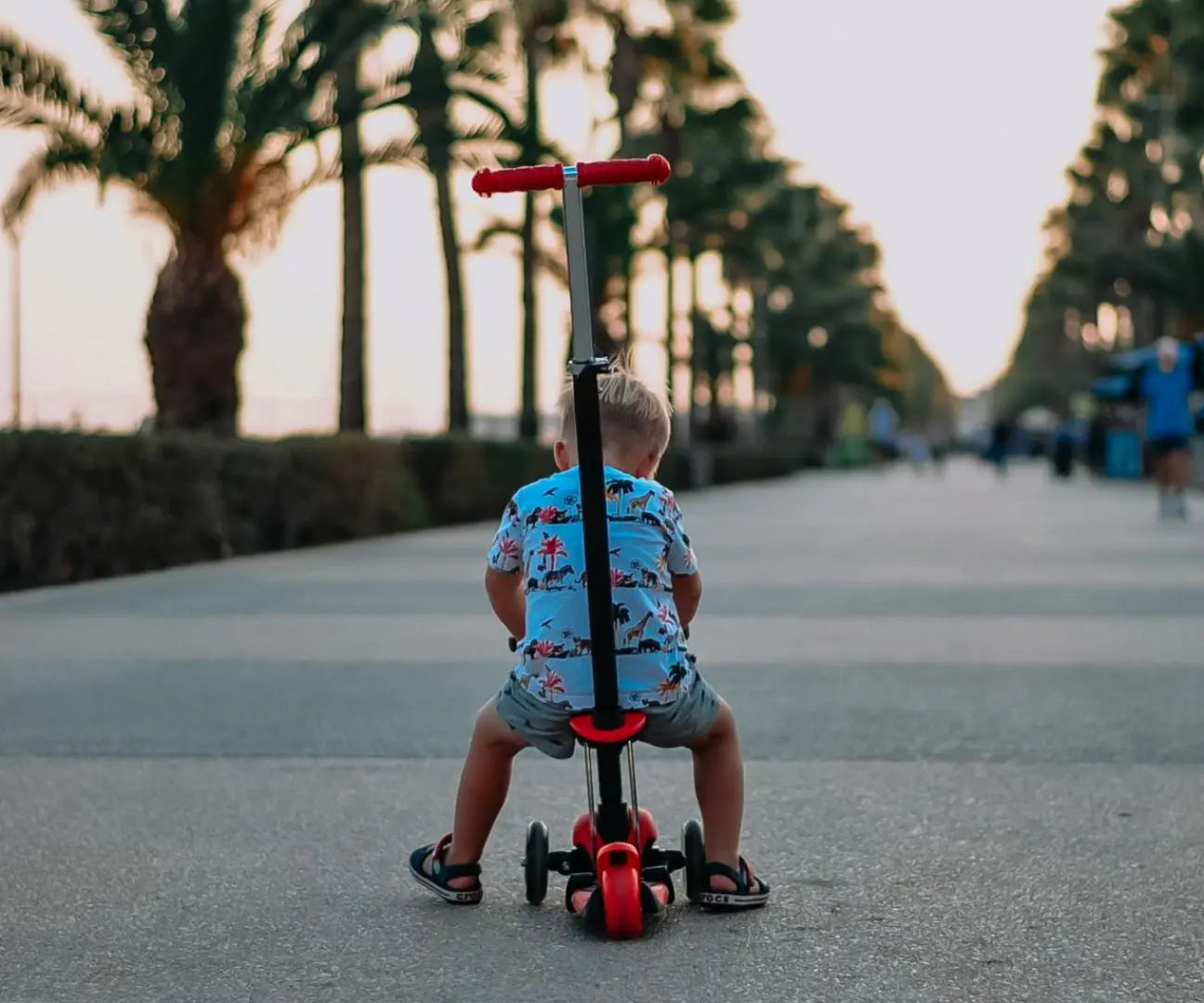 A toddler on a 3-in-1 scooter with a seat and adjustable handlebar. Front wheels light up, suitable for children from 18 months. Safety gear recommended.