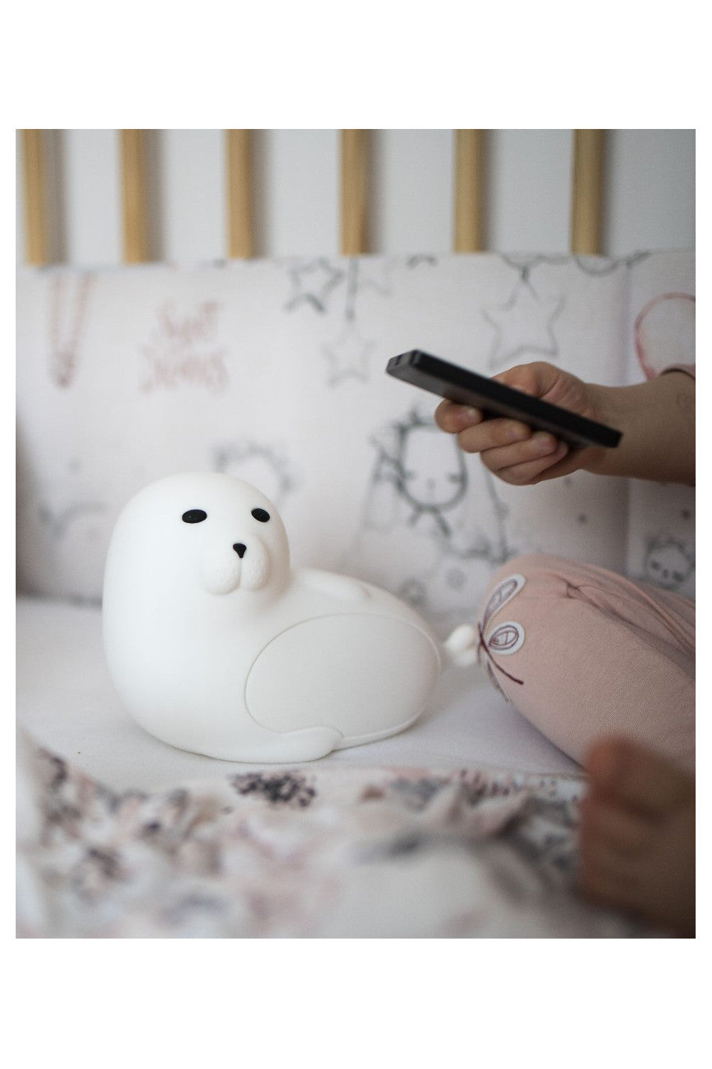 Person holding remote control for white seal toy lamp, featuring soft silicone, 7 color lights, touch activation, USB-C charging, and child-friendly remote functions.