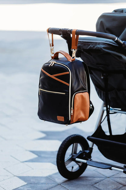 A black and brown backpack with stroller straps, featuring multiple pockets, a laptop compartment, and thermal lining for bottles. Designed for parents on the go by Ally Scandic.