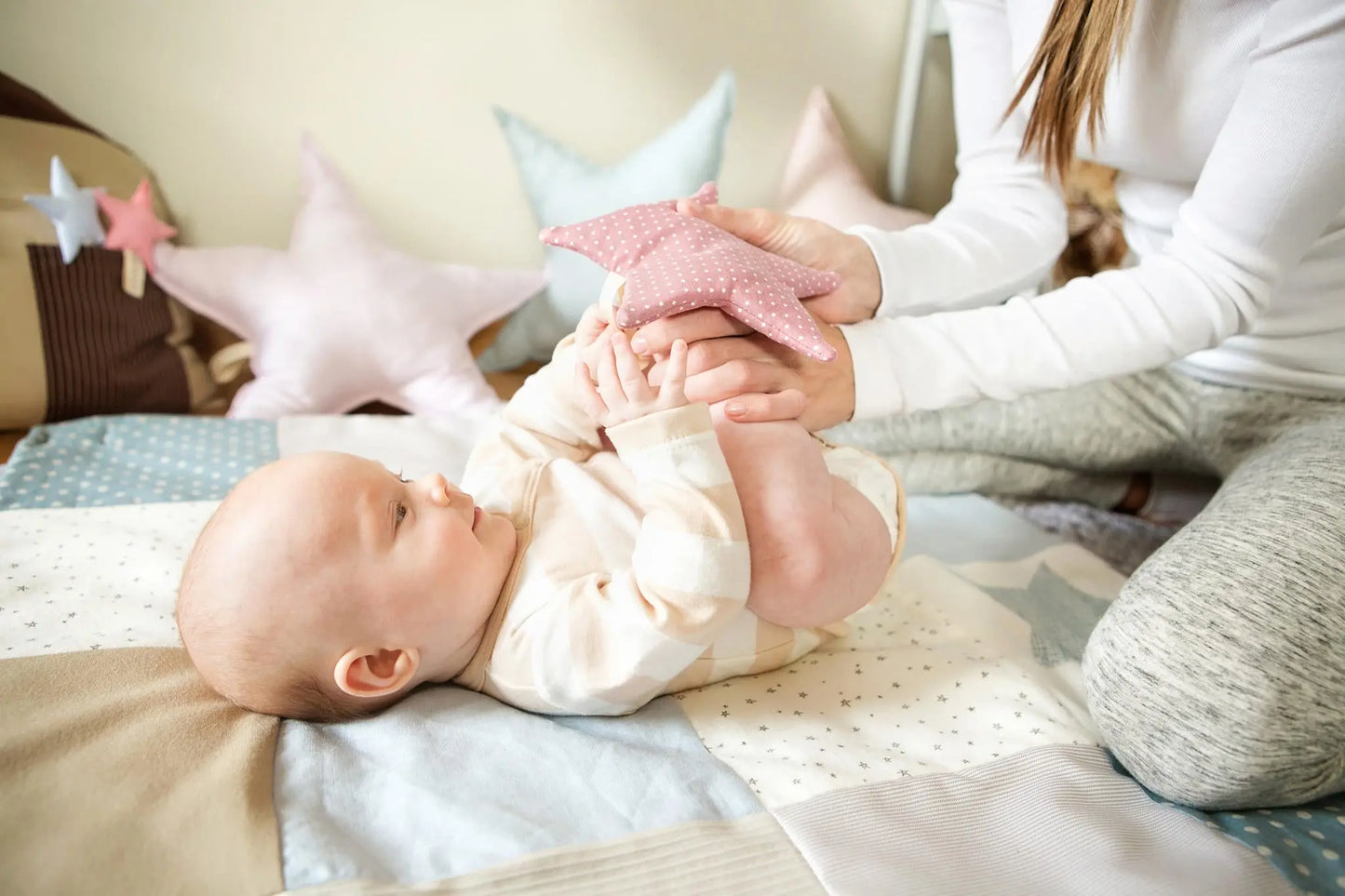 A baby interacts with star-shaped toys on a blue activity mat with detachable arches. Stimulates sensory exploration and motor skills development.