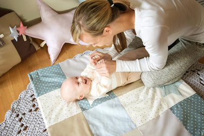 A woman holding a baby on a Small Baby Activity Mat with interactive arches and starry sky design. Includes 3 toys and ecologic cotton material.