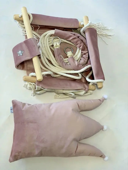 A pink pillow and rope with a crown-shaped cushion swing in Dusty Pink, designed for children's rooms. Made of velvet plush, pinewood, and cotton ropes for comfort and durability.