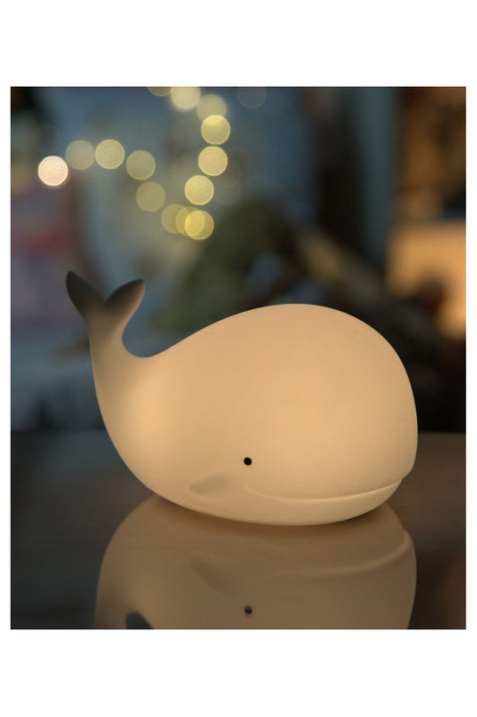 A white whale-shaped lamp with a remote control, soft silicone material, and multi-color lighting options for children's comfort and safety.