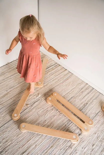 A toddler stands on a wooden balance beam, promoting balance and coordination. Crafted from safe plywood, this set includes three beams and connectors for developmental play.