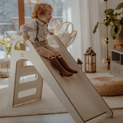 Child on wooden indoor Scandi Slide, 87x46cm, with three steps, stable structure, and comfortable handles for safe play and motor skill development.