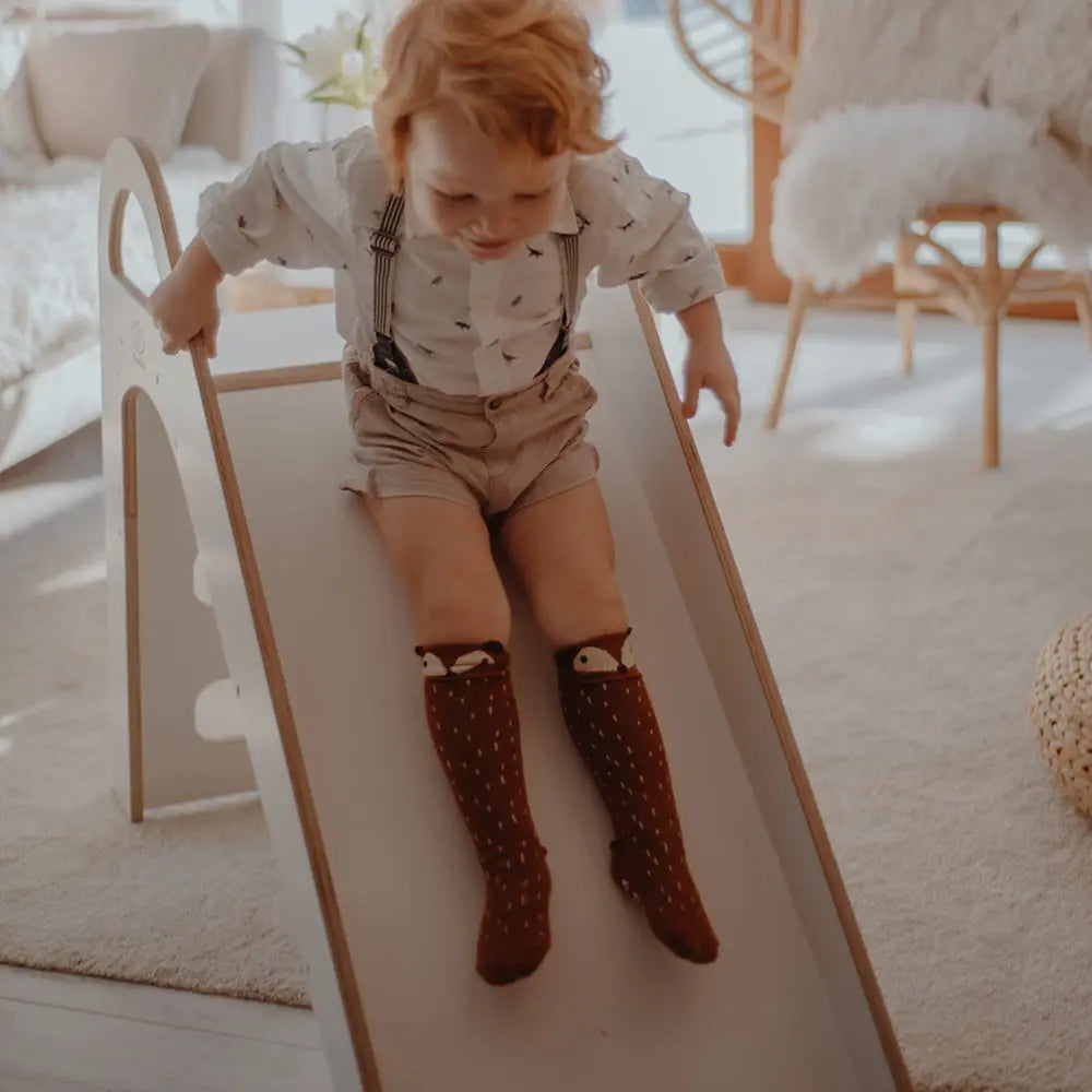 Child on Wooden Indoor Scandi Slide, 87x46cm, with stable structure, 3 steps, and comfortable handles for safe play, promoting motor skills and balance.