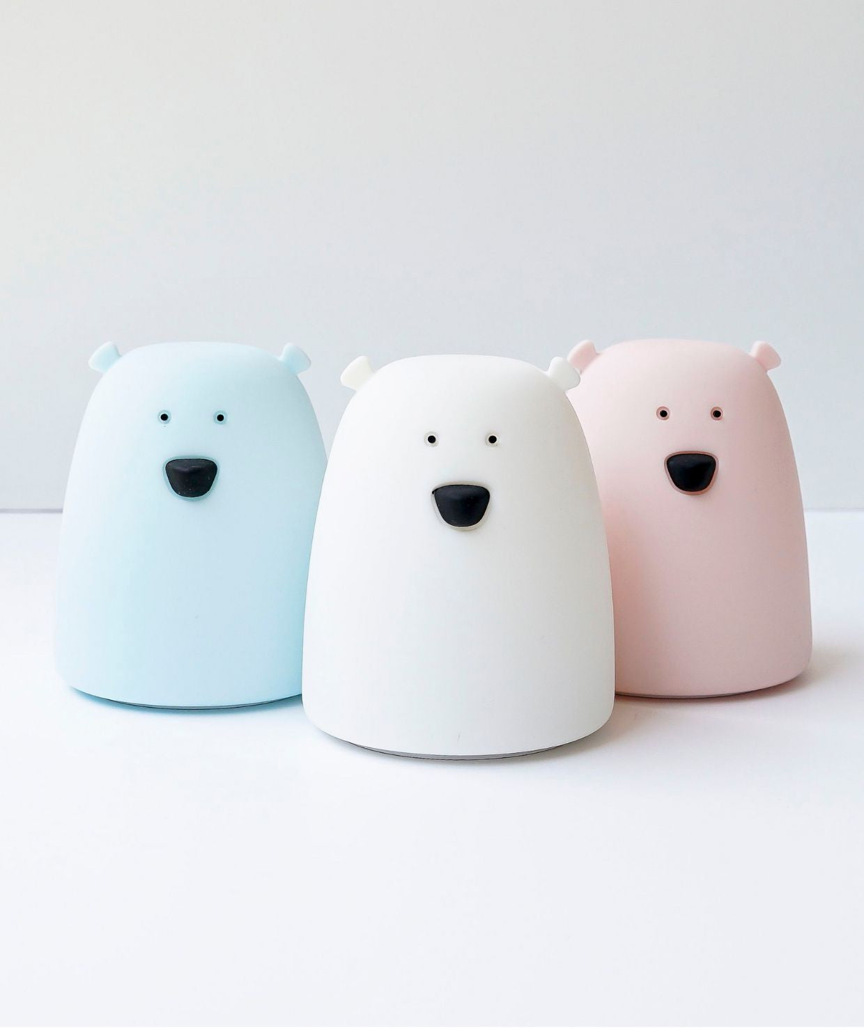 A group of white bear toys, including a close-up view, symbolizing the Little Bear Silicone Lamp. Soft, touchable, battery-powered night light for kids, shining in 7 colors, with a 12-hour operation time.