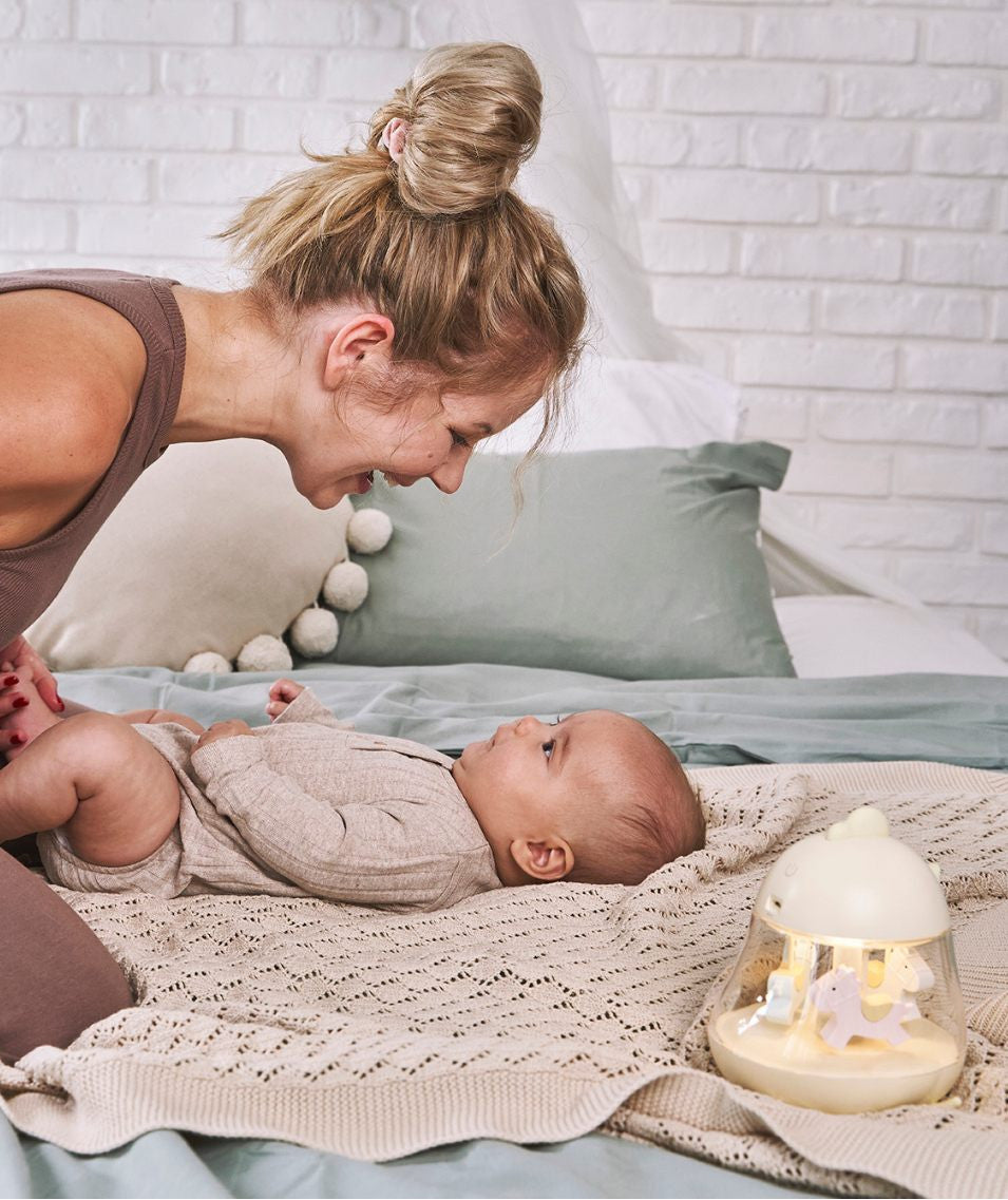 A woman plays with a baby near a white toy horse inside a lamp with a carousel and music box. Lamp features include a merry-go-round design, soothing melody, color-changing light, and USB charging.