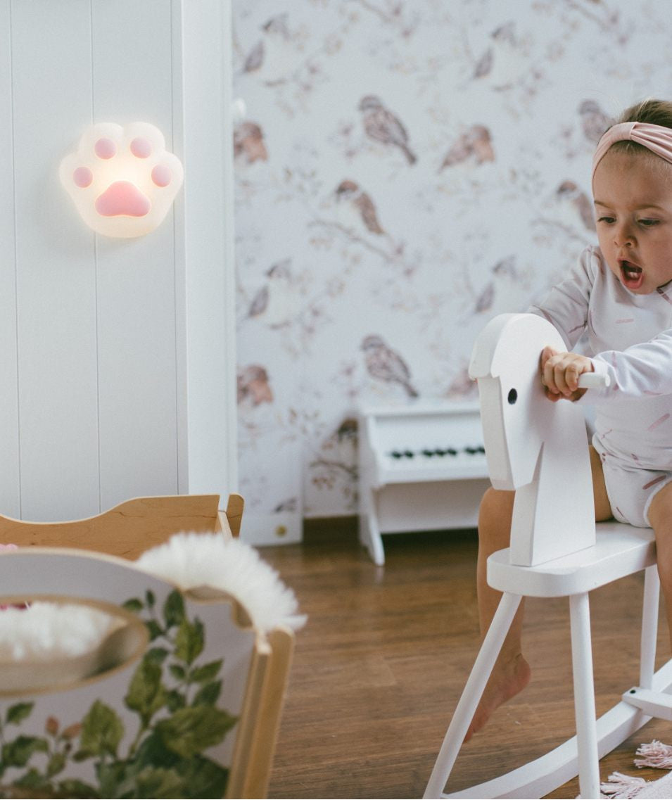 A child on a toy horse, a baby on a rocking horse, and a girl playing with a toy horse, all captured in the Paw Silicone Lamp - Pink, a soft, touch-operated night light for children's rooms.