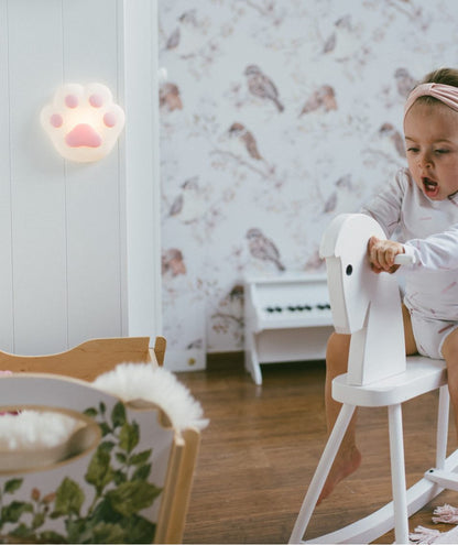 A child on a toy horse, a baby on a rocking horse, and a girl playing with a toy horse, all captured in the Paw Silicone Lamp - Pink, a soft, touch-operated night light for children's rooms.