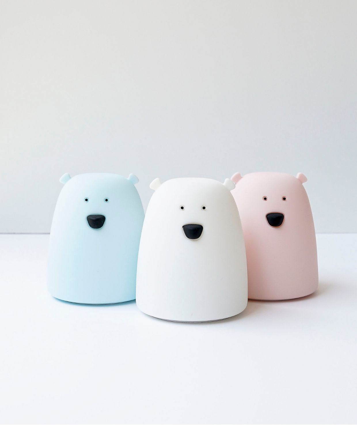 A group of small plastic bears, including a white bear toy with a black nose and ears, and a close-up of a toy, representing the Little Bear Silicone Lamp - White, a soft, touch-operated night light for children.