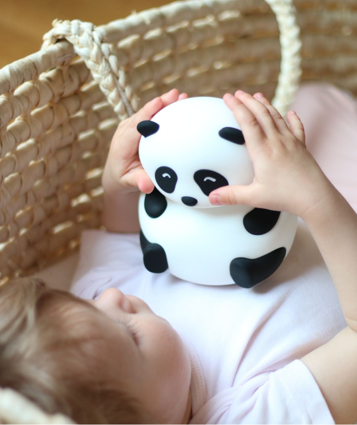 A baby lies in a crib with a toy panda, showcasing the Panda Silicone Lamp. Soft, touchable, and safe for children, it lights up in 7 colors, charges via USB Type-C, and offers 12 hours of light.