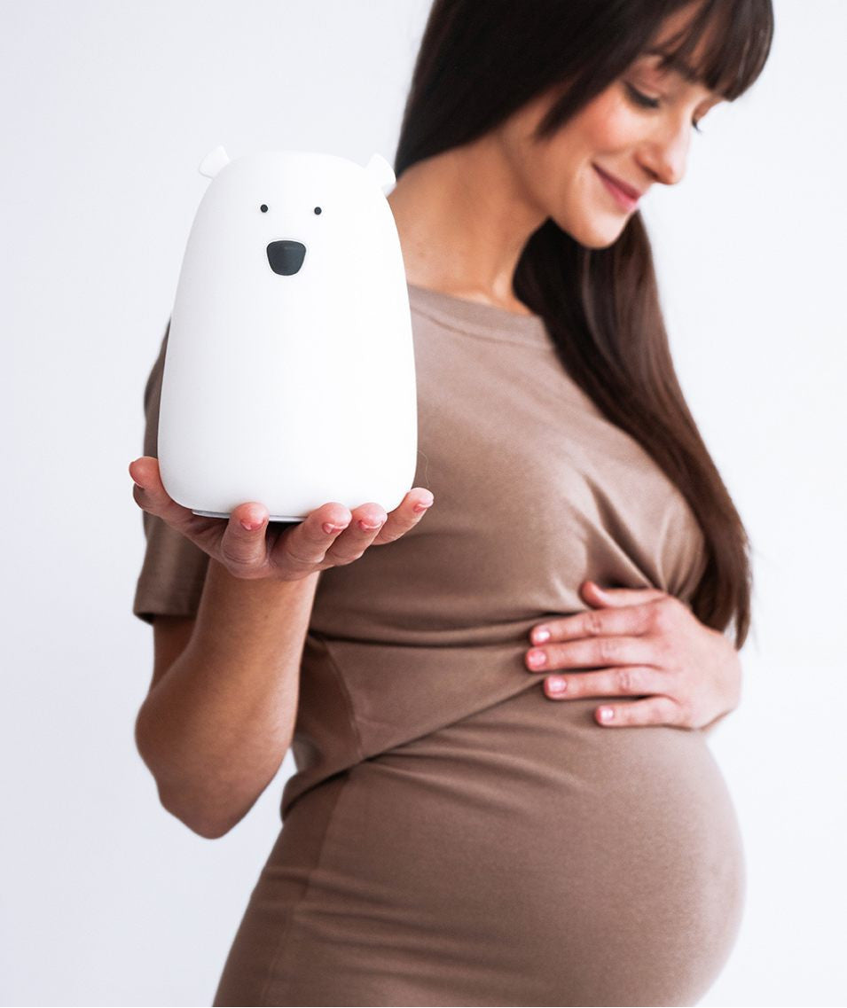 A pregnant woman holds a white Bear lamp from Rabbit & Friends, featuring a charming teddy bear shape with black eyes and nose. Soft, touch-responsive, and portable for bedtime routines.