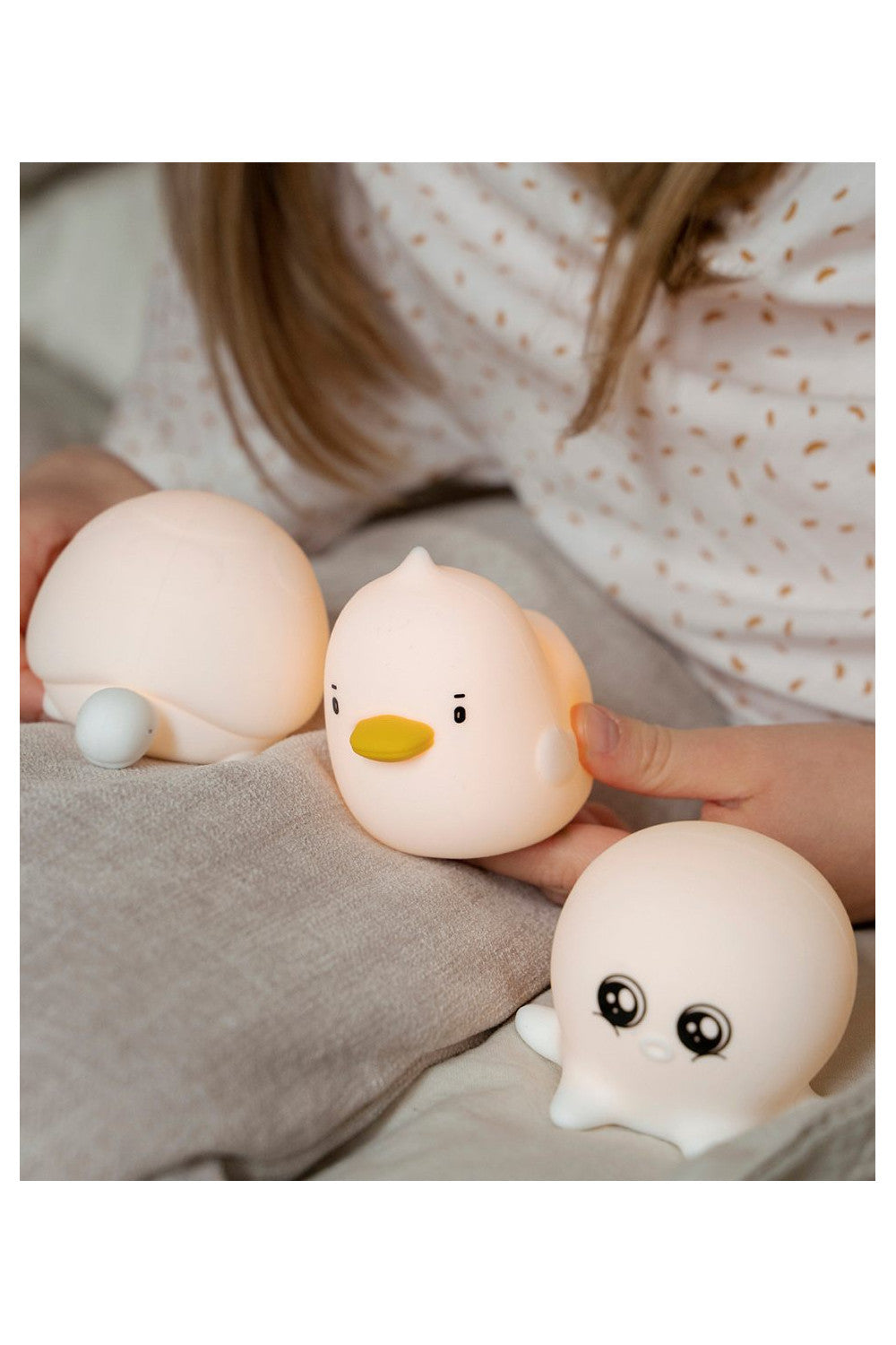 A person holding a small white duck toy and a white round toy with black eyes, part of a waterproof set of 3 mini aquatic silicone lamps for children's rooms.