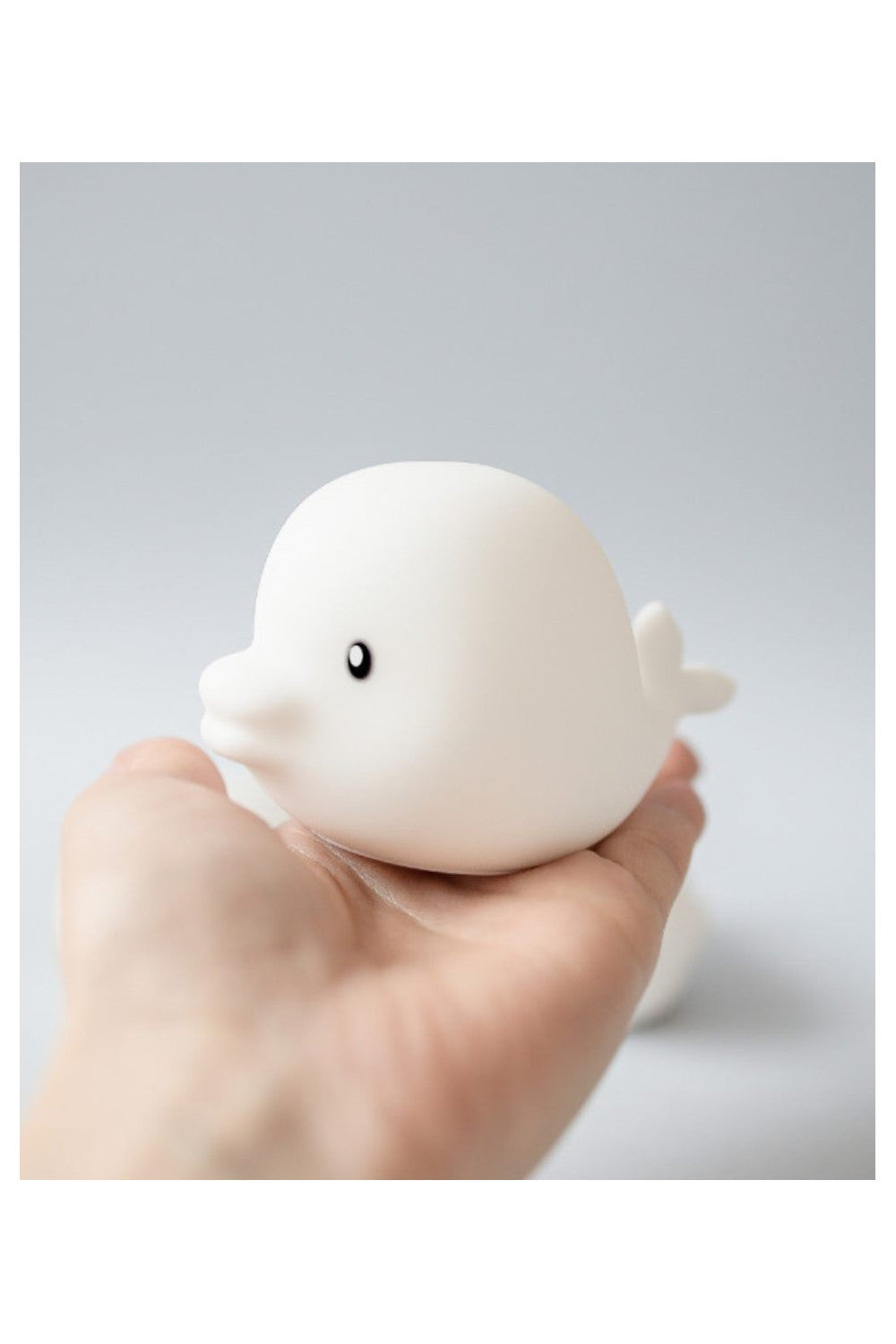 A hand holding a white waterproof set of 3 mini marine silicone lamps in charming shapes of Dolphin, Whale, and Shark. Soft silicone skin, color-changing light, and IP67 waterproof rating.