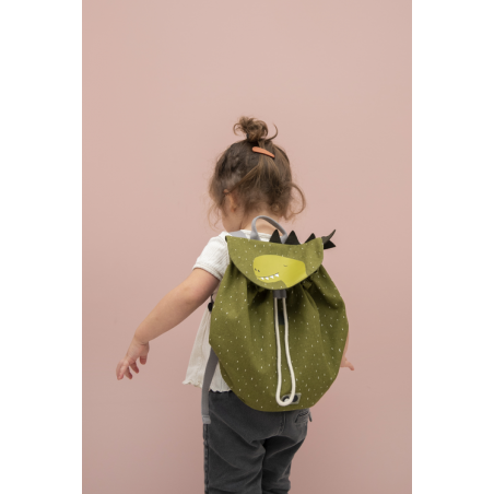 A child with a green mini drawstring backpack featuring a cartoon dinosaur. Roomy, water repellent, washable, perfect for adventures. Dimensions: 30 x 23 cm, 5L capacity. Age recommendation: 3+.