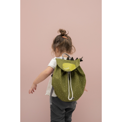 A child with a green mini drawstring backpack featuring a cartoon dinosaur. Roomy, water repellent, washable, perfect for adventures. Dimensions: 30 x 23 cm, 5L capacity. Age recommendation: 3+.