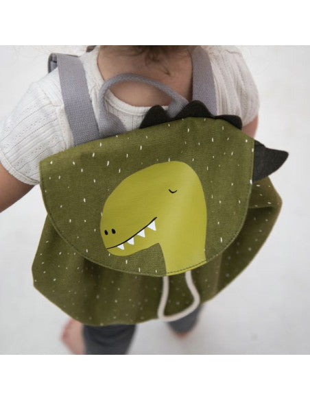 Child wearing a mini drawstring backpack featuring a green dinosaur face with sharp teeth. Roomy, water-repellent, and washable. Ideal for adventures. Dimensions: 30 x 23 cm. Capacity: 5 l. Recommended for ages 3+.