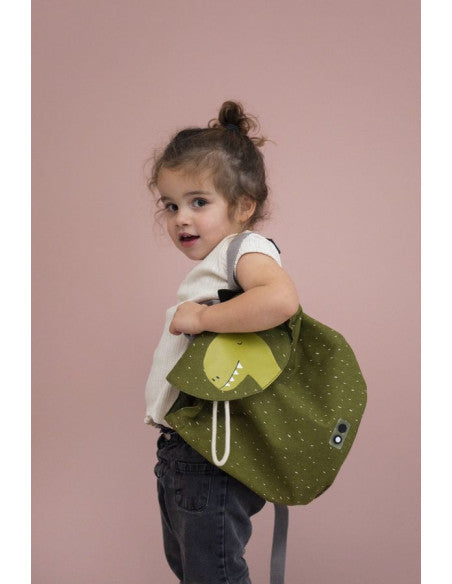 A child holding a green Mini Drawstring Backpack - Mr Dino, perfect for adventures. Water repellent, washable, 100% cotton material, 5L capacity, ideal for ages 3+. Dimensions: 30 x 23 cm.