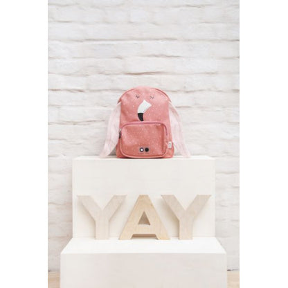 A pink Mrs. Flamingo backpack with face detail, adjustable straps, chest strap, water-repellent cotton material, big compartment, and front pocket. Dimensions: 31 x 23 x 10 cm.