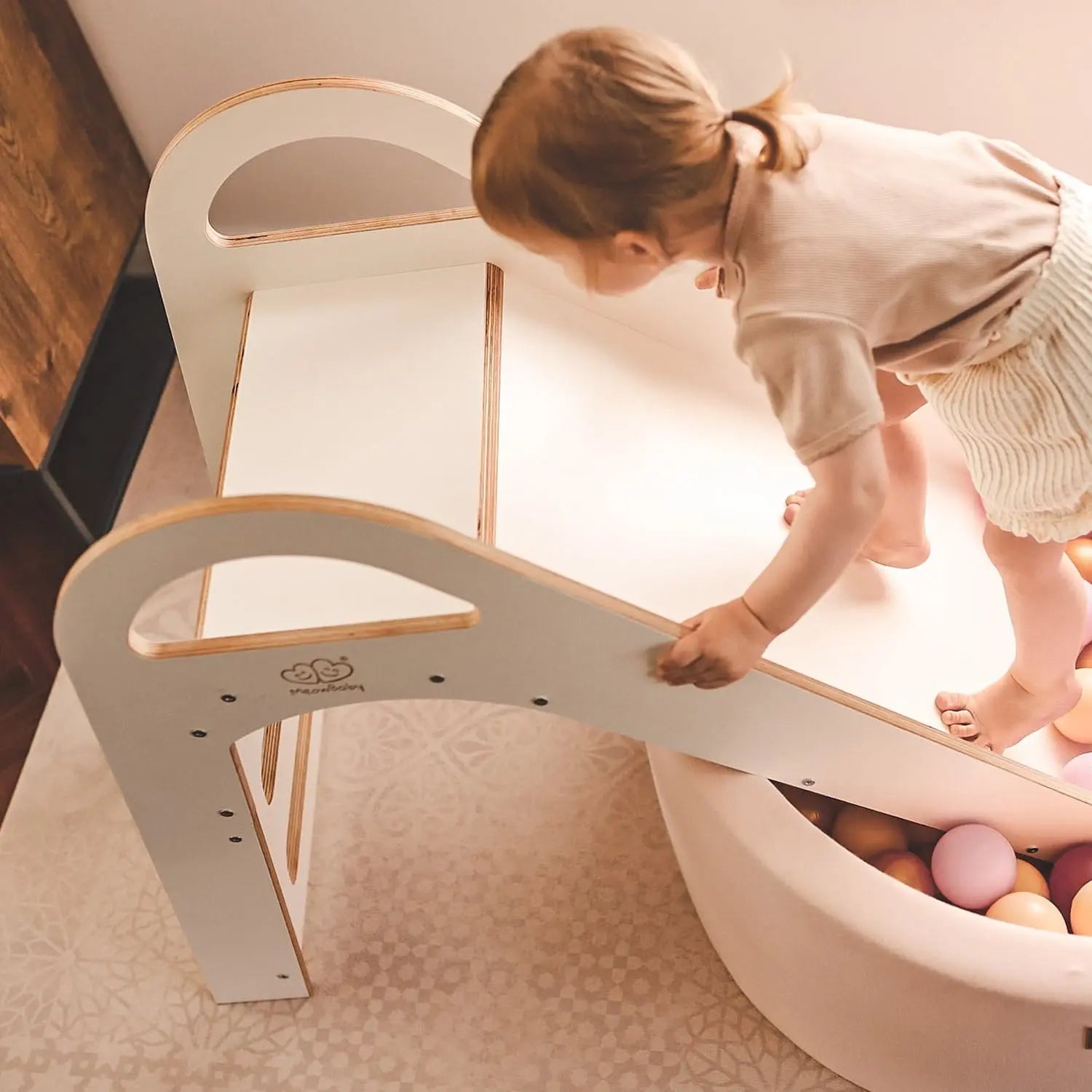 A child climbing a wooden indoor Scandi slide, 87x46cm, with stable structure, smooth edges, and comfortable handles for safe play. Ideal for toddlers over 12 months.